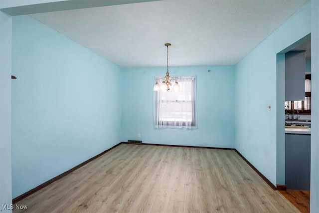 unfurnished dining area with light wood finished floors, a notable chandelier, baseboards, and a sink