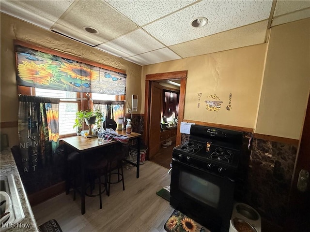 kitchen with a paneled ceiling, wainscoting, wood finished floors, and gas stove