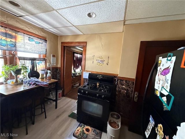 kitchen featuring a wainscoted wall, black appliances, wood finished floors, and a paneled ceiling