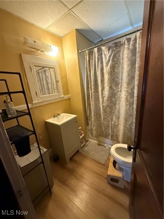 full bath featuring a drop ceiling, a shower with shower curtain, toilet, wood finished floors, and vanity