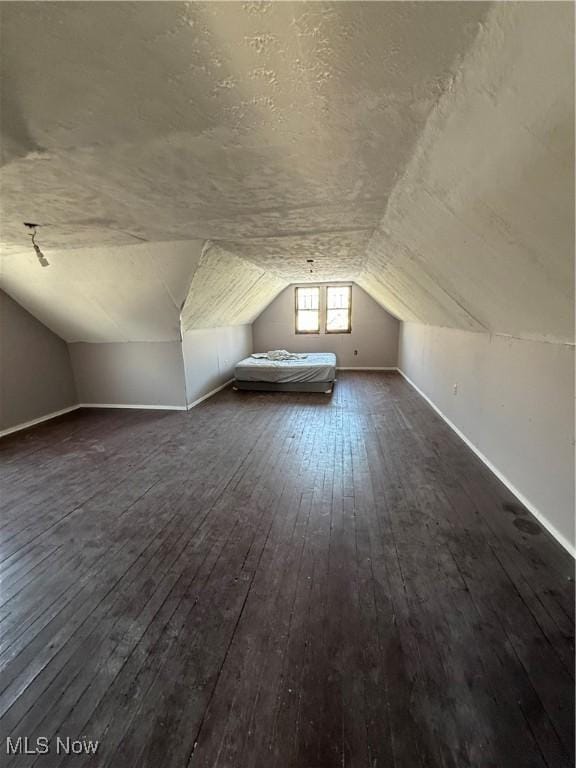 bonus room featuring lofted ceiling, dark wood-type flooring, a textured ceiling, and baseboards