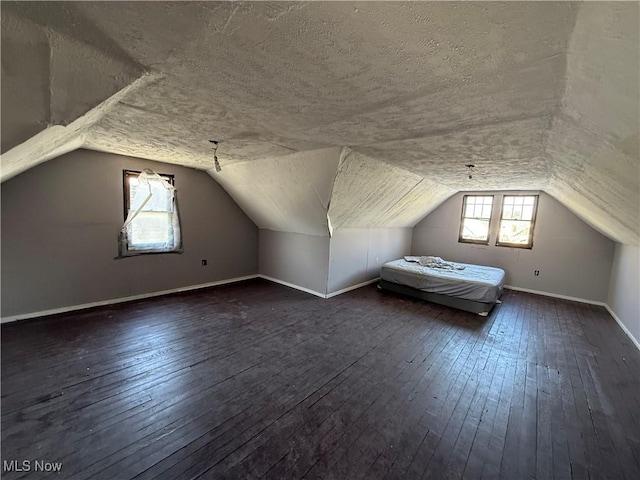 additional living space with dark wood-style floors, baseboards, vaulted ceiling, and a textured ceiling