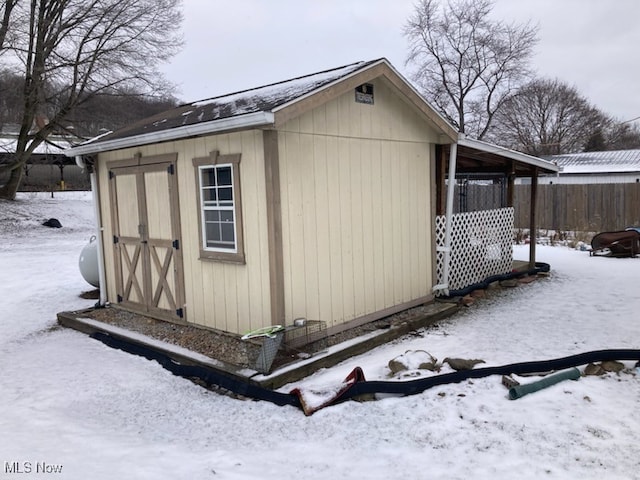 snow covered structure featuring a shed, fence, and an outbuilding