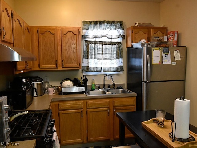 kitchen featuring under cabinet range hood, brown cabinetry, a sink, and freestanding refrigerator