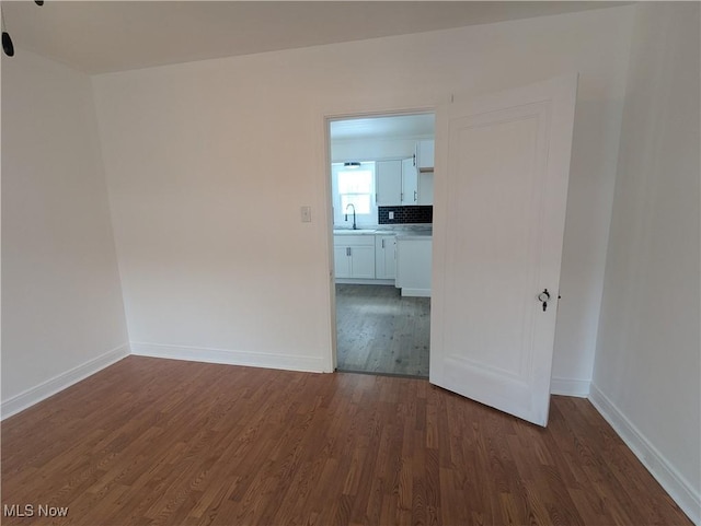 spare room featuring dark wood-style floors, a sink, and baseboards