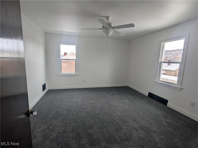 spare room featuring a ceiling fan, dark carpet, visible vents, and baseboards