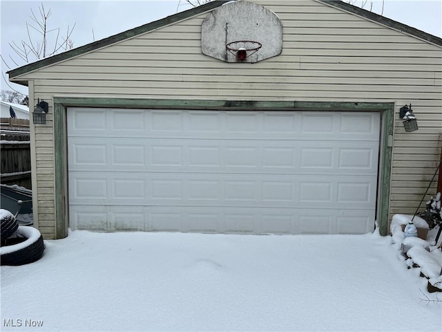 snow covered garage featuring a detached garage and fence