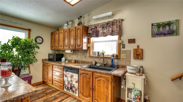 kitchen with stainless steel dishwasher, brown cabinetry, vaulted ceiling, a sink, and black microwave