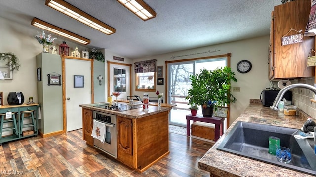 kitchen with black electric cooktop, a sink, stainless steel oven, dark wood-style floors, and brown cabinetry