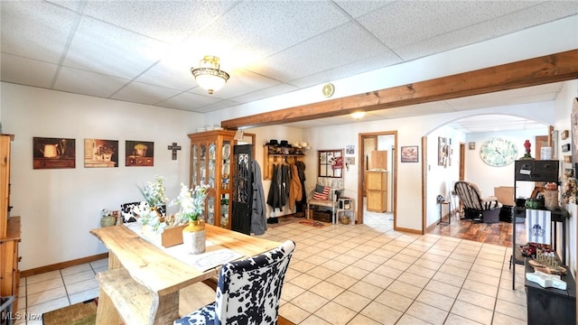 tiled dining area with arched walkways, a paneled ceiling, and baseboards