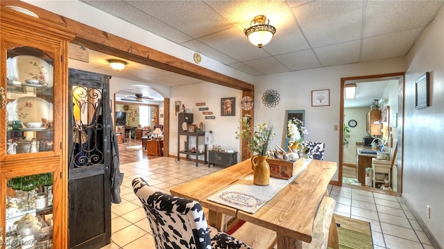 dining area with baseboards, arched walkways, a ceiling fan, a paneled ceiling, and light tile patterned flooring