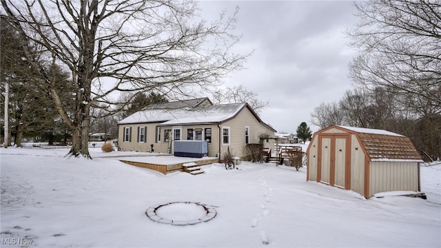 snow covered rear of property featuring an outbuilding, a wooden deck, and a storage unit