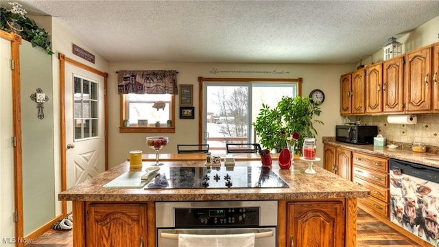 kitchen with a kitchen island with sink, light countertops, brown cabinets, black appliances, and tasteful backsplash