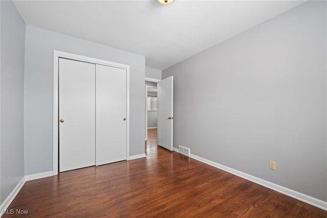 unfurnished bedroom with a closet, dark wood finished floors, visible vents, and baseboards