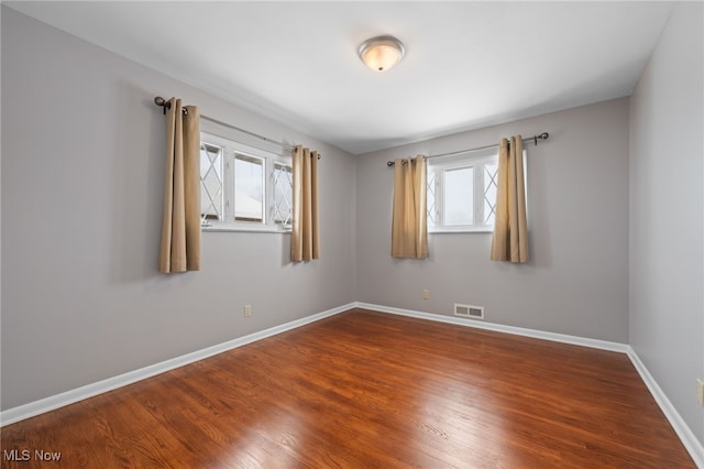 spare room featuring wood finished floors, visible vents, and baseboards