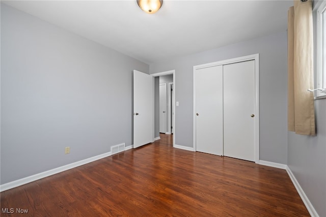 unfurnished bedroom with baseboards, visible vents, dark wood finished floors, and a closet