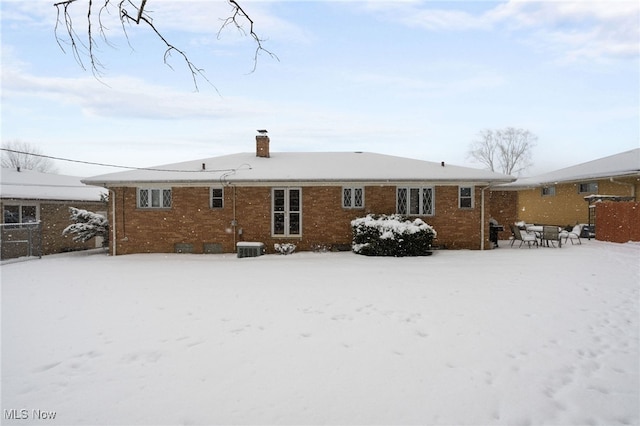 snow covered back of property featuring brick siding, a chimney, and central air condition unit