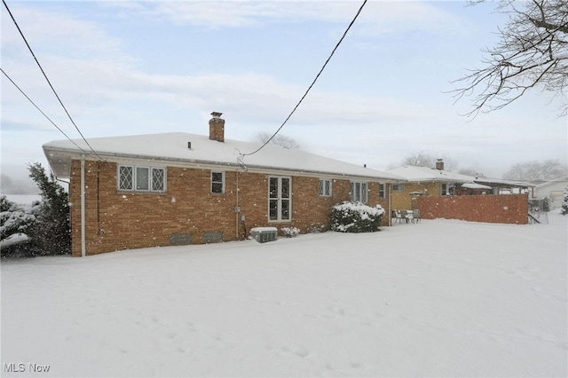 snow covered house featuring brick siding and a chimney