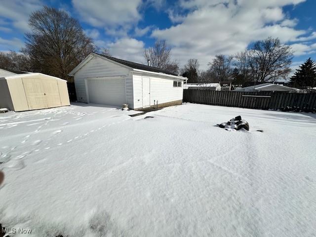 snow covered garage with a garage and fence