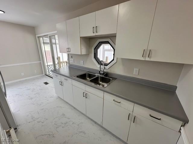 kitchen with marble finish floor, dark countertops, a sink, and white cabinetry