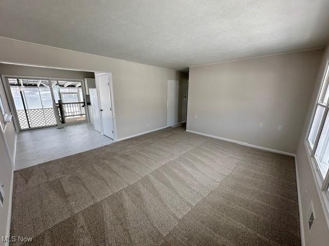 empty room featuring a textured ceiling, carpet flooring, and baseboards