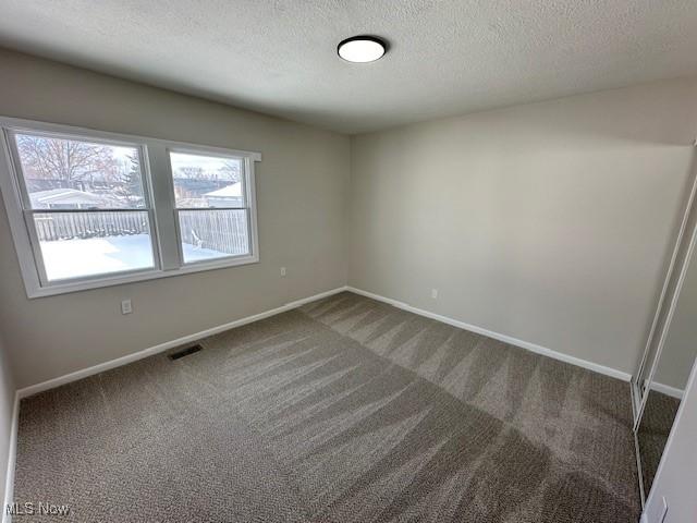 carpeted spare room featuring baseboards, visible vents, and a textured ceiling