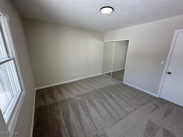 unfurnished bedroom featuring a textured ceiling, a closet, carpet, and baseboards