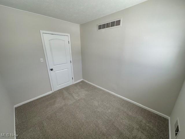 carpeted spare room featuring visible vents, a textured ceiling, and baseboards