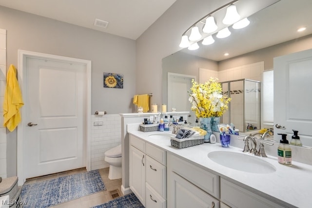 full bathroom with tile walls, visible vents, toilet, a stall shower, and a sink