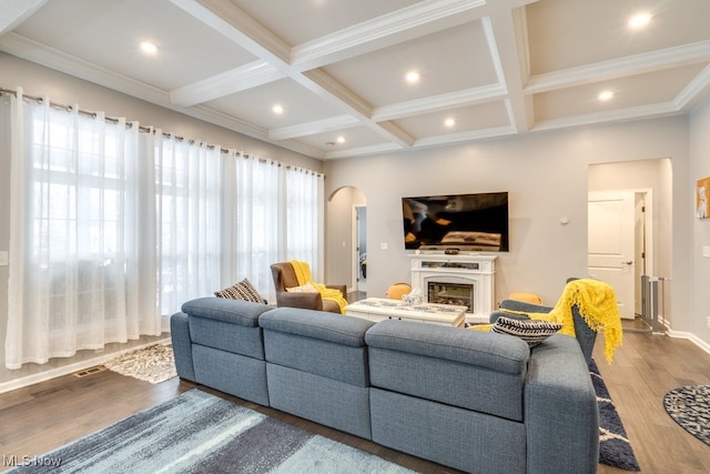 living room with arched walkways, coffered ceiling, wood finished floors, beamed ceiling, and a fireplace