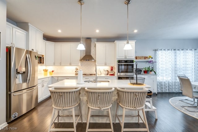 kitchen featuring stainless steel appliances, light countertops, wall chimney range hood, and an island with sink