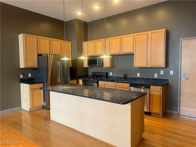 kitchen with light wood finished floors, hanging light fixtures, appliances with stainless steel finishes, and a kitchen island