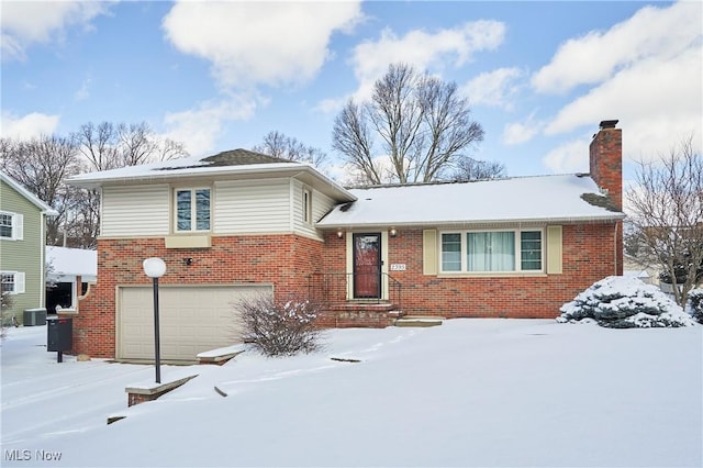 tri-level home with brick siding, a chimney, an attached garage, and central air condition unit