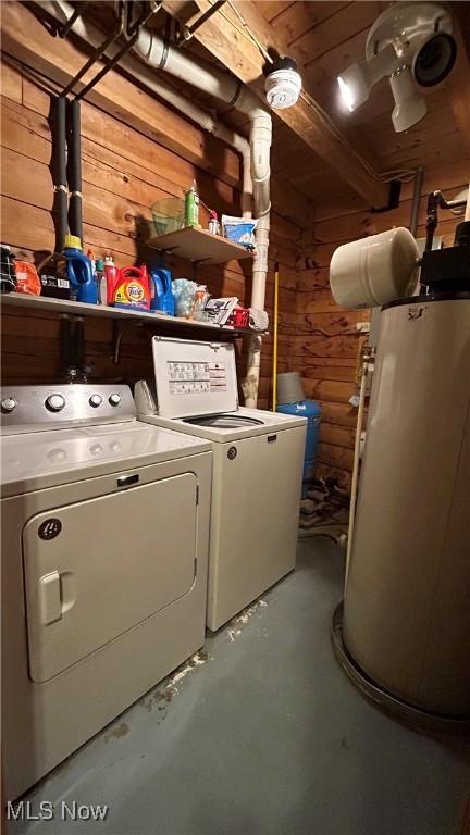 laundry area featuring laundry area, water heater, wood walls, and separate washer and dryer