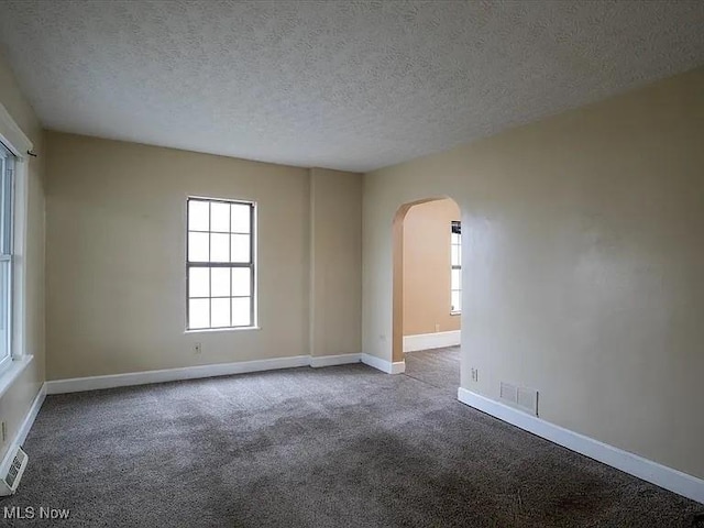 spare room with arched walkways, visible vents, carpet flooring, a textured ceiling, and baseboards