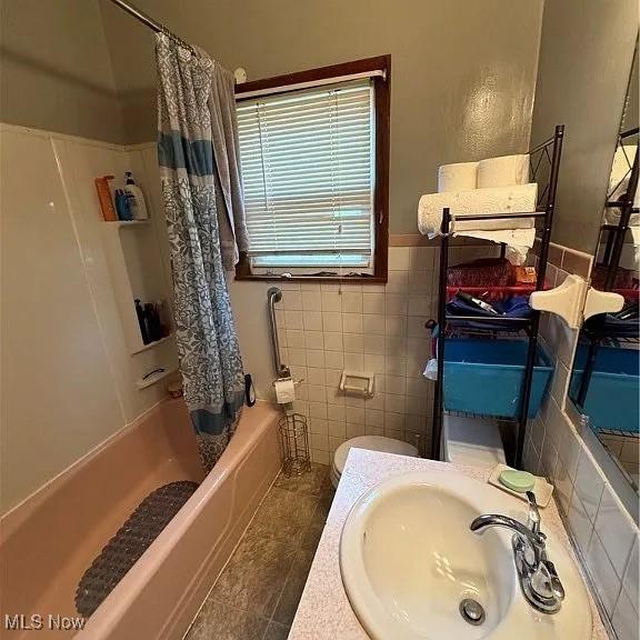 full bathroom featuring toilet, tile patterned floors, a sink, shower / bathtub combination with curtain, and tile walls