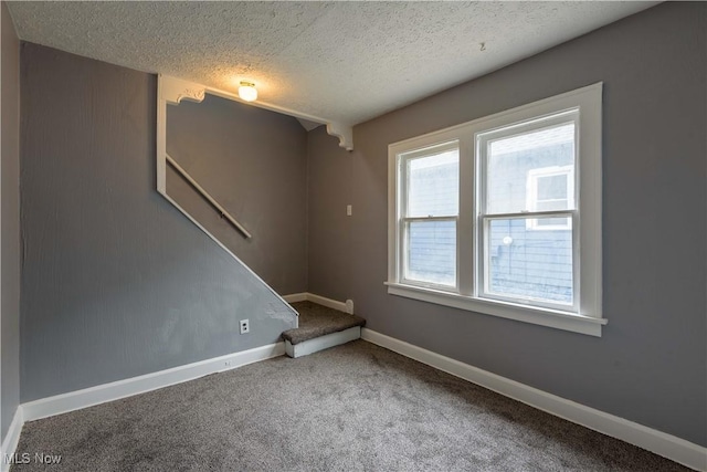 carpeted spare room with a textured ceiling, baseboards, and stairs