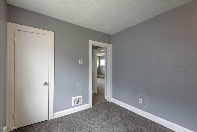 unfurnished bedroom featuring a textured ceiling, dark carpet, visible vents, and baseboards