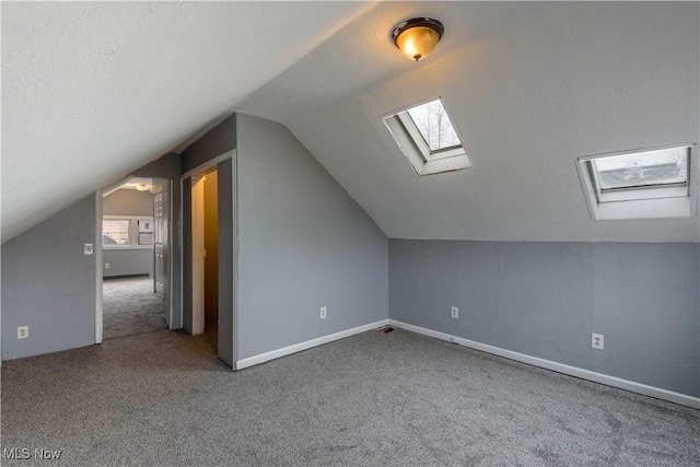 additional living space featuring carpet floors, lofted ceiling with skylight, a textured ceiling, and baseboards