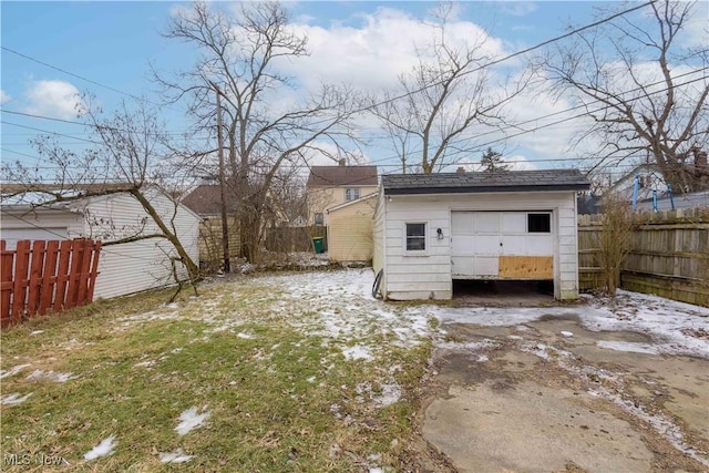 rear view of property featuring a detached garage, fence, and an outbuilding