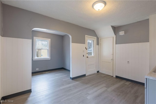 interior space featuring a textured ceiling, a wainscoted wall, lofted ceiling, and light wood-style floors