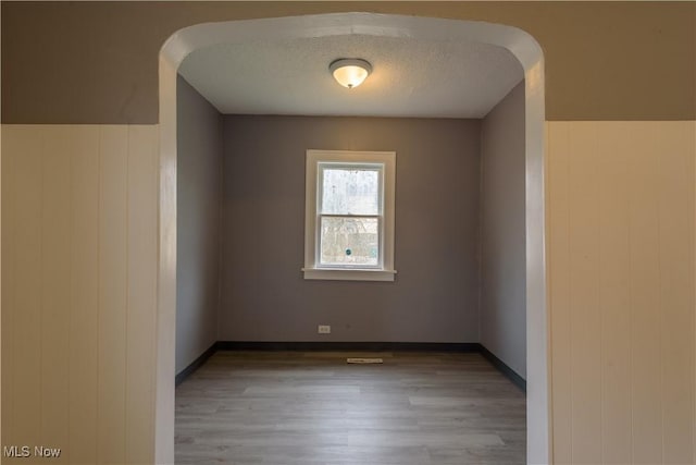 spare room with light wood-style flooring, baseboards, and a textured ceiling