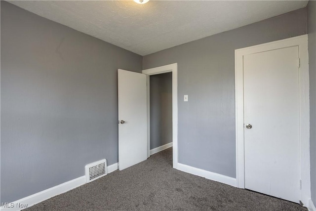 unfurnished bedroom with baseboards, visible vents, dark carpet, and a textured ceiling