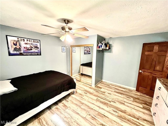 bedroom featuring a closet, ceiling fan, a textured ceiling, light wood-type flooring, and baseboards