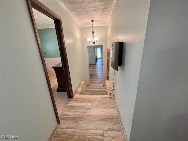 hallway with ornamental molding, light wood-style floors, baseboards, and an inviting chandelier