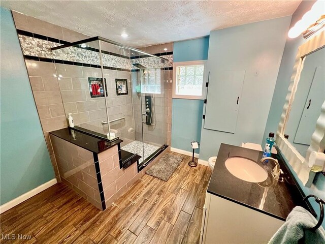 bathroom with a stall shower, a textured ceiling, baseboards, and wood finished floors