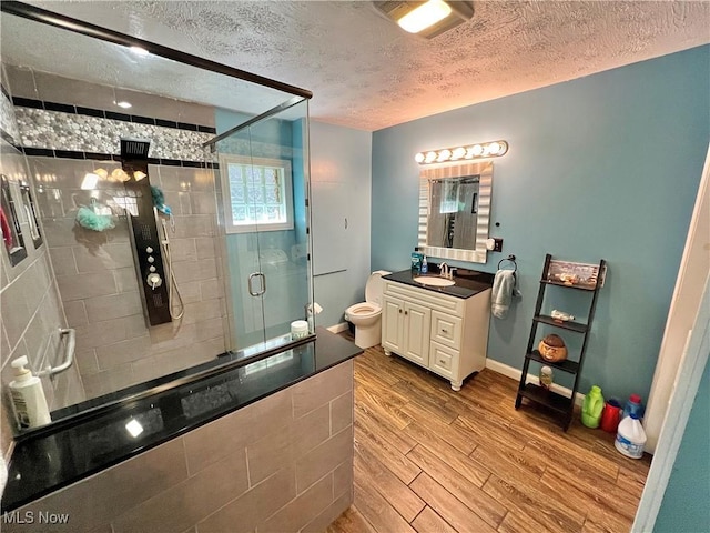 bathroom with toilet, wood finished floors, a textured ceiling, vanity, and a shower stall