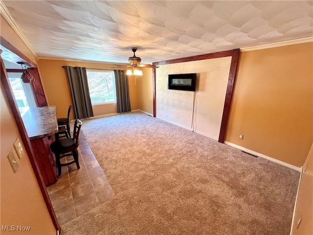 interior space with carpet floors, baseboards, ornamental molding, and a ceiling fan