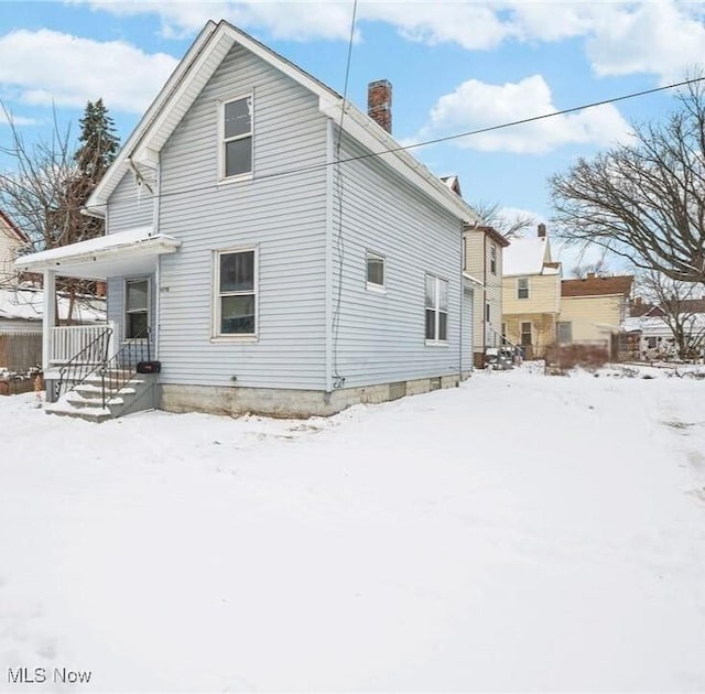 snow covered house with a porch and a chimney