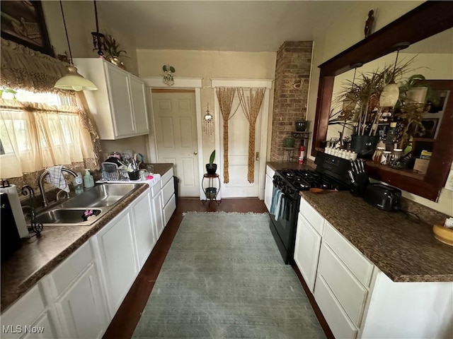 kitchen featuring dark countertops, hanging light fixtures, white cabinets, a sink, and black stove